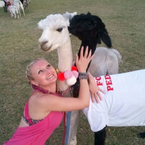 girl with pink tank top hugging two alpacas