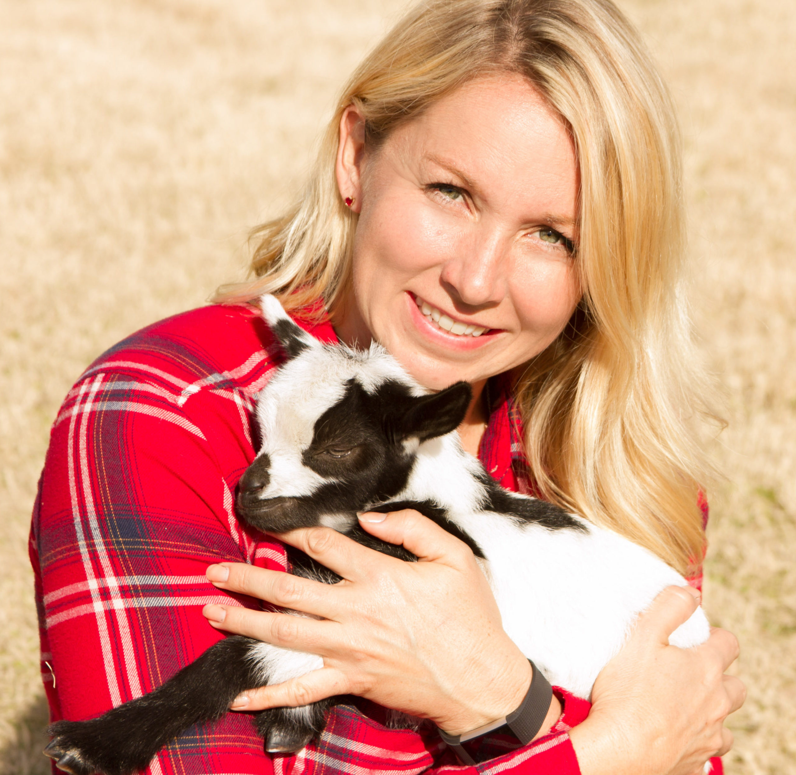 Sarah in a plaid shirt holding a baby goat with yoga